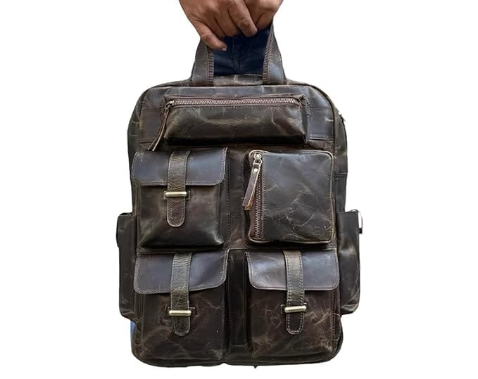A brown leather backpack with multiple compartments and brass buckles, being held by a person.