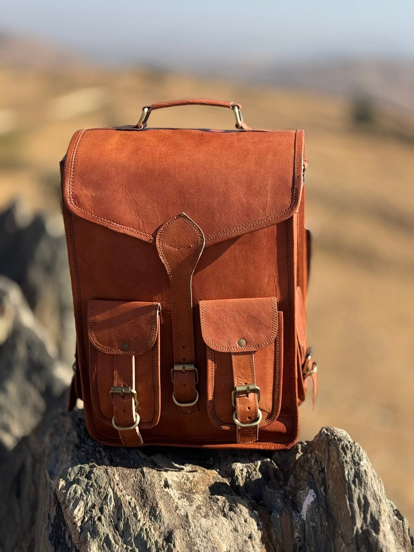 A tan brown leather shoulder cum backpack bag with multiple compartments. The Design of bag is Aesthetic. 