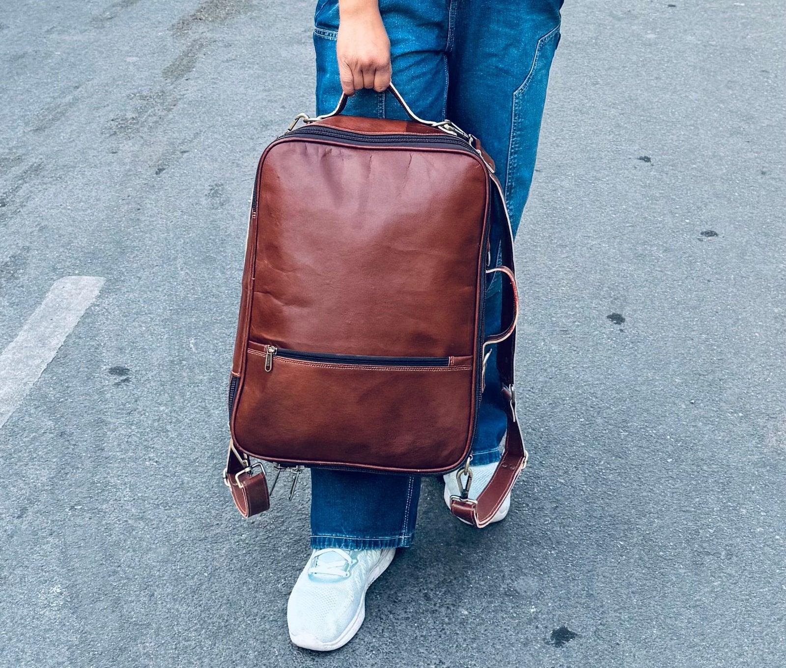 A person carrying a Unisex brown leather laptop backpack on their back.