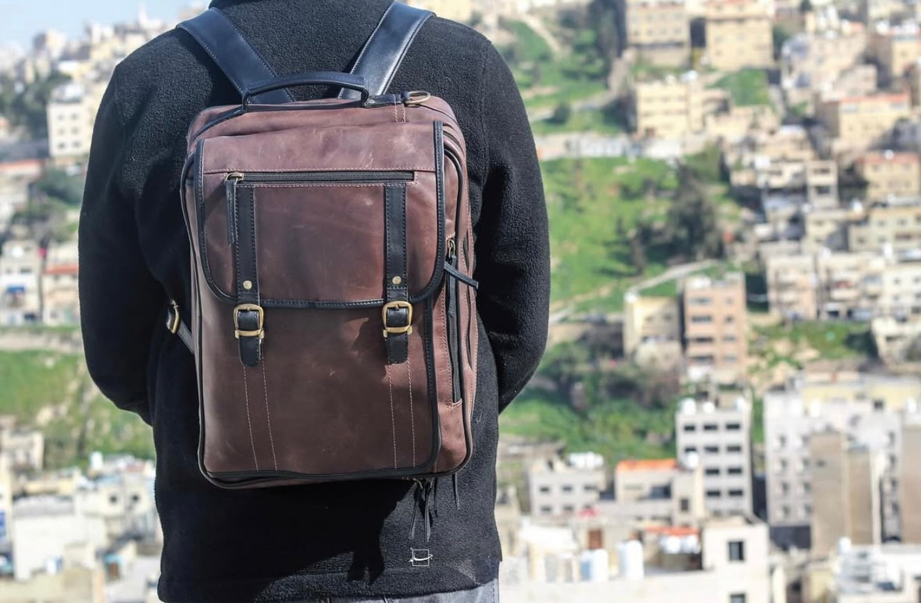 A person wearing a brown full grain leather backpack cum shoulder bag over their shoulders.